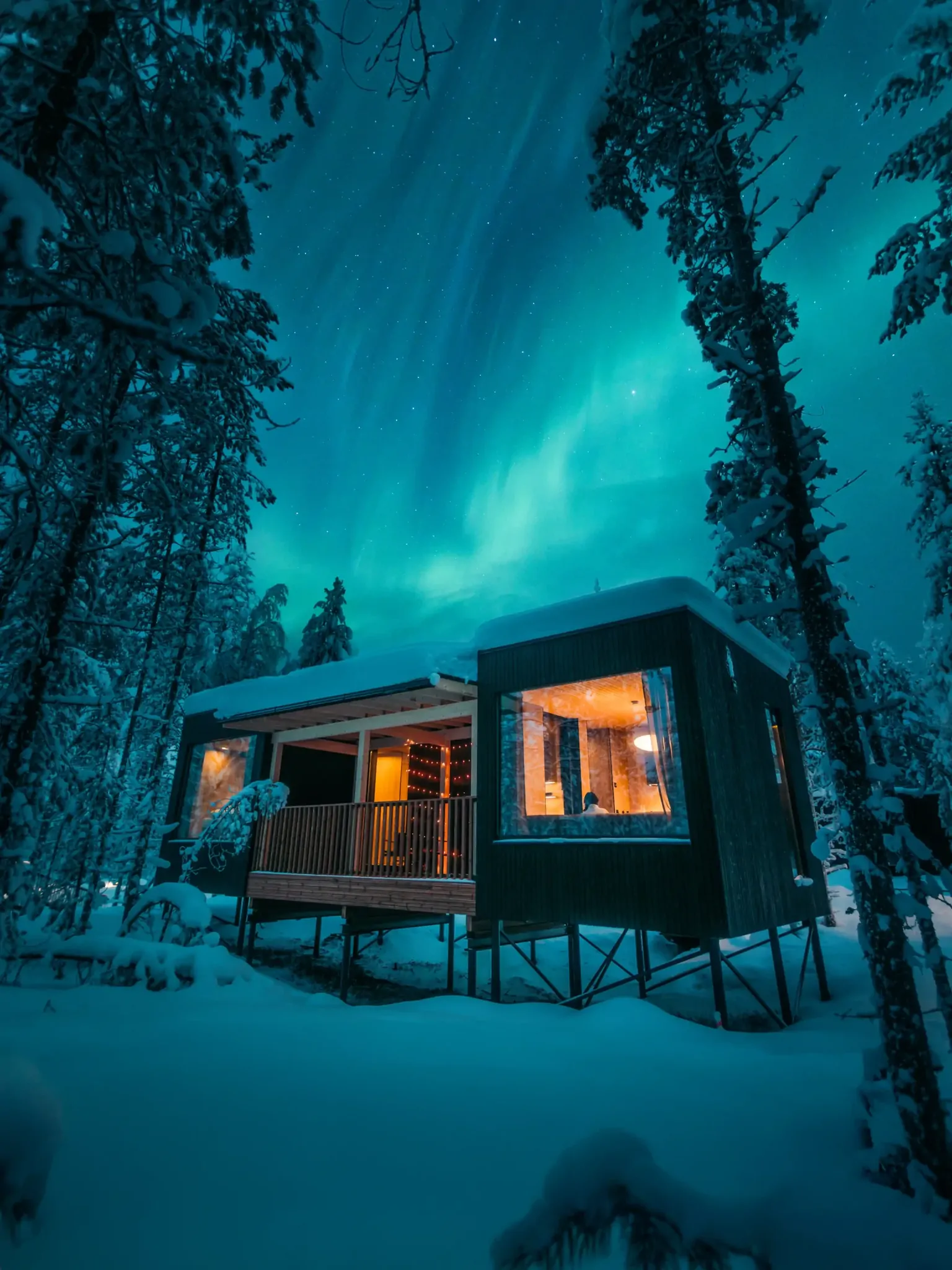 Northern lights over a lit villa in the snowy forest